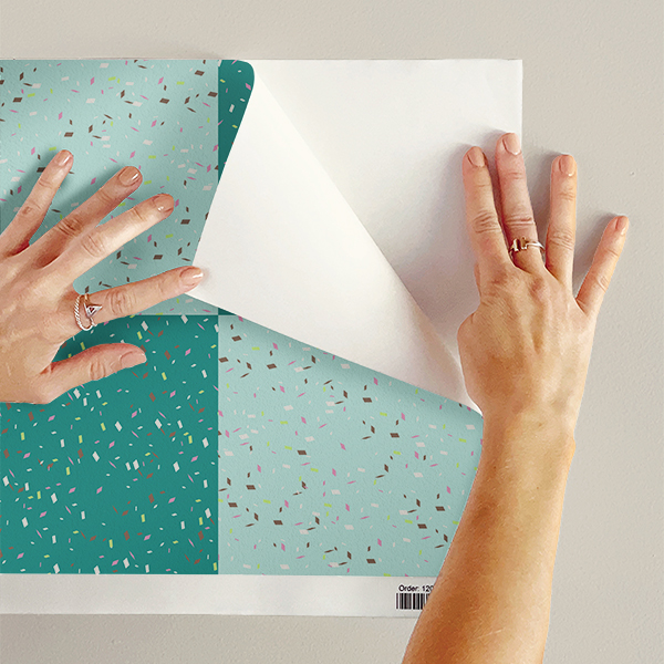 The artwork features a repeating geometric pattern of symmetrical shapes resembling elongated, curved diamonds or petals in various shades of blue and green. Each shape is split vertically with one half filled with a light blue and the other half filled with green or darker blue. The background is a light, almost pastel blue, which provides a soft yet vibrant backdrop. One of the blue shapes near the upper left contains a white starburst element, adding a focal point of brightness to the composition. The overall design conveys a modern, mid-century aesthetic with clean lines and harmonious color contrasts.
